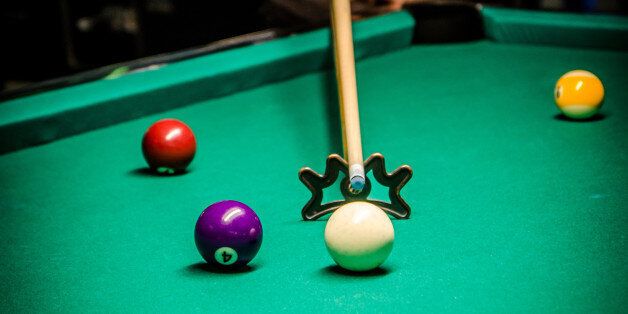 Young and pretty woman using bridge stick to hit cue ball during pool game