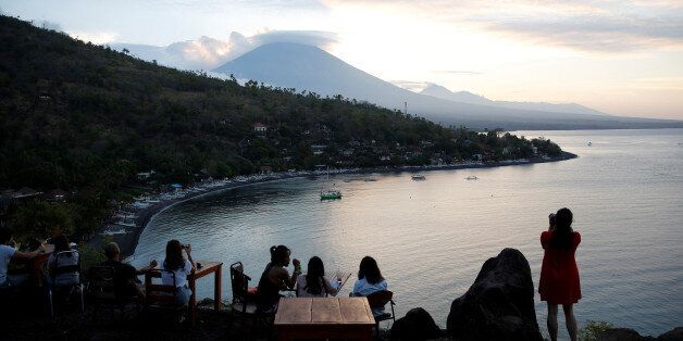 Tourists have a drink while watching the sunset behind Mount Agung, a volcano on the highest alert level, in Amed on the resort island of Bali, Indonesia September 25, 2017. REUTERS/Darren Whiteside