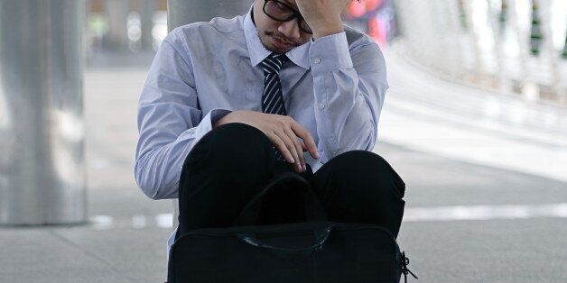 Portrait of frustrated stressed young Asian man sitting on the floor of sidewalk office and feeling tired with job