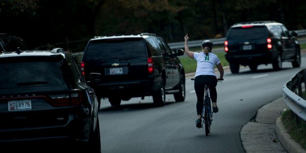 TOPSHOT - A woman on a bike gestures with her middle finger as a motorcade with US President Donald Trump departs Trump National Golf Course October 28, 2017 in Sterling, Virginia. / AFP PHOTO / Brendan Smialowski        (Photo credit should read BRENDAN SMIALOWSKI/AFP/Getty Images)