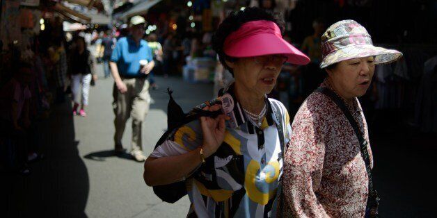 Elderly women wearing sun visors walk in a market in Seoul on May 30, 2014. Sun visors are a familiar sight during the summer months in South Korea, which places a high importance on UV protection and skin care. AFP PHOTO / Ed Jones        (Photo credit should read ED JONES/AFP/Getty Images)