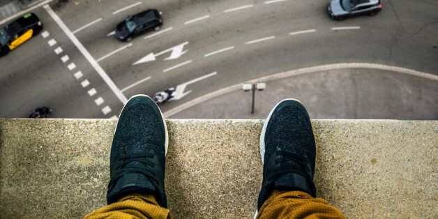 Two feet at the edge of a rooftop of a high building. A busy street appears looking down.