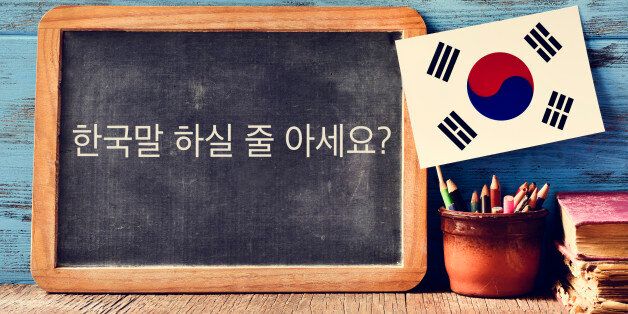 a chalkboard with the question do you speak Korean? written in Korean, a pot with pencils, some books and the flag of South Korea, on a wooden desk