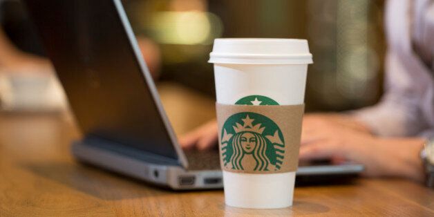 The Starbucks Corp. logo sits on a carboard coffee cup as a customer uses a laptop computer inside a Starbucks Corp. coffee shop in London, U.K., on Monday, June 9, 2014. U.K. services companies' confidence rose to a record this quarter, indicating continued expansion in the largest part of the economy, the Confederation of British Industry said. Photographer: Jason Alden/Bloomberg via Getty Images