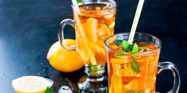 Refreshing Iced Tea with lemon in two glass cups on black background, copy space