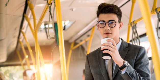 pensive young businessman in eyeglasses drinking coffee to go in bus