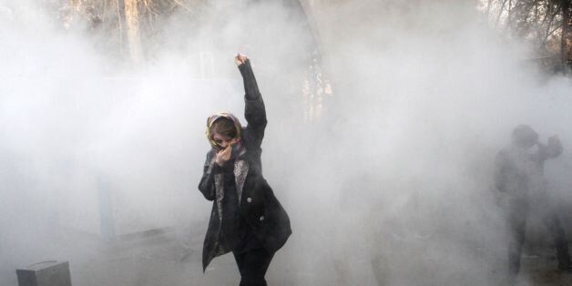 TOPSHOT - An Iranian woman raises her fist amid the smoke of tear gas at the University of Tehran during a protest driven by anger over economic problems, in the capital Tehran on December 30, 2017.Students protested in a third day of demonstrations sparked by anger over Iran's economic problems, videos on social media showed, but were outnumbered by counter-demonstrators. / AFP PHOTO / STR        (Photo credit should read STR/AFP/Getty Images)