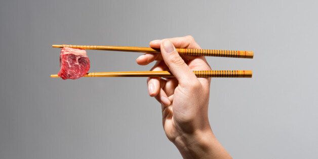 Young woman's hand holding a cube of raw beef with chop sticks