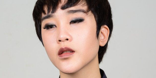 Studio shot of young Asian transgender teenage boy against gray background horizontal shot