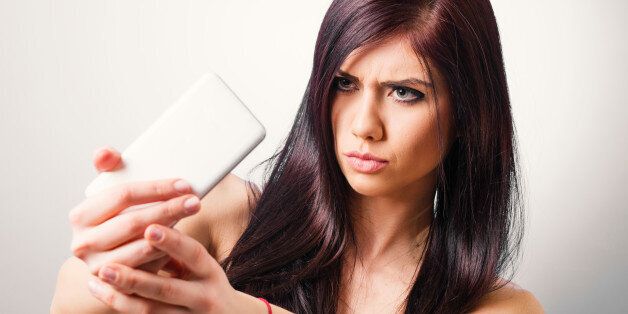 Beautiful young brunette taking selfie with smart phone - studio shot