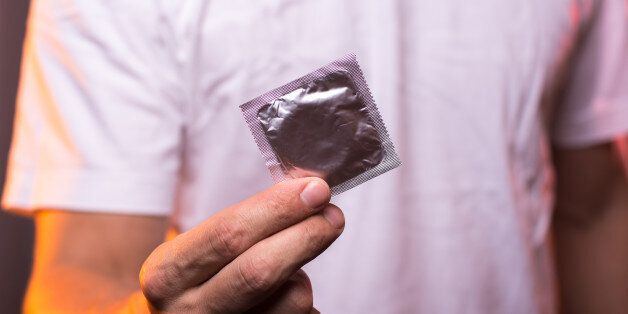Unknown man in white shirt holding condom in hand, closeup.