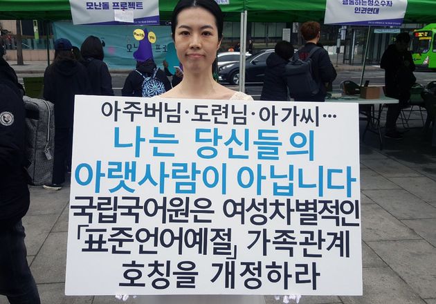 4일 결혼식 피로연에서 입었던 하얀 드레스를 입고 서울 종로구 광화문 광장에 선 배윤민정씨가 '아주버님·도련님·아가씨…나는 당신들의 아랫사림이 아닙니다'라는 피켓을 들고 국립국어원에 여성차별적인 표준어를 개정하라고 촉구하고 있다. 