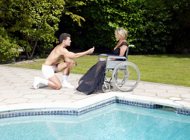 젊은 남성이 휠체어를 탄 중년 여성에게 프로포즈를 하고 있다. 바로 옆에는 수영장이 있다.
