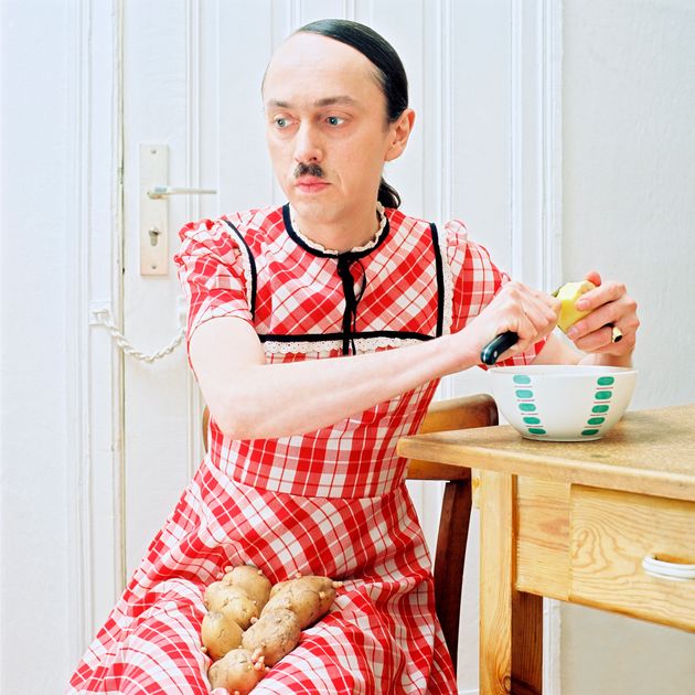 아돌프 히틀러의 얼굴을 한 남성이 여성의 옷을 입고 감자를 깎고 있다. 