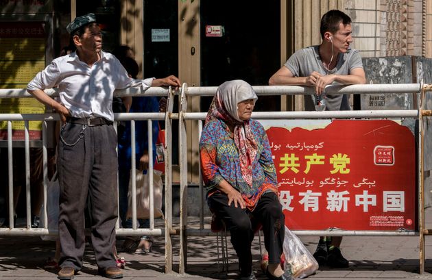 위구르인들이 버스를 기다리는 모습. 배경에 있는 광고판에는 '공산당 없이 새로운 중국은 없을 것'이라는 문구가 적혀있다. 우루무치, 신장위구르자치구, 중국. 2016년 6월18일.