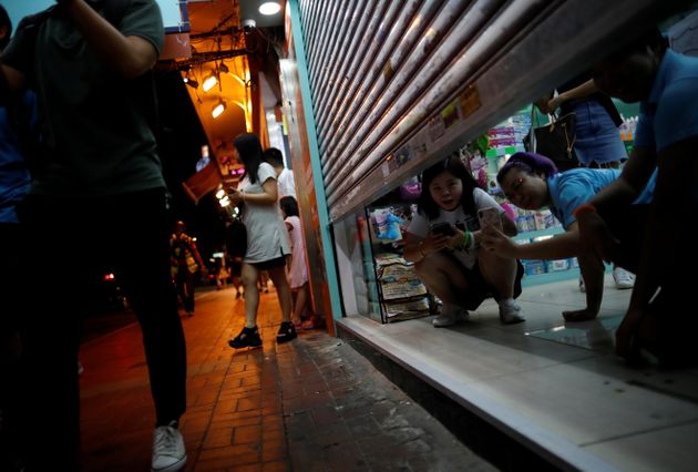 거의 다 내려진 셔터 틈으로 사진을 찍는 주민들의 모습. 홍콩. 2019년 8월17일.