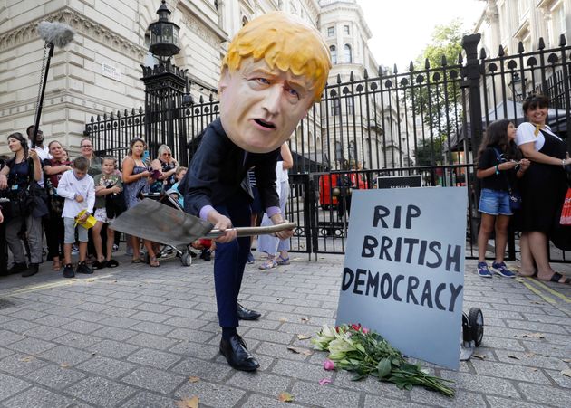 보리스 존슨 총리 탈을 쓴 한 시민이 영국 총리관저 앞에서 '영국 민주주의의 죽음'이라는 문구가 적힌 비석을 앞에 두고 항의 퍼포먼스를 벌이고 있다. 런던, 영국. 2019년 8월28일.