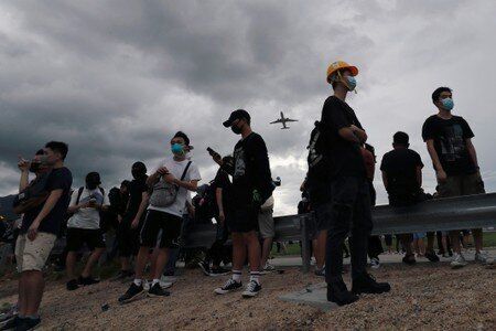 A plane flies over anti-extradition bill protesters as they demonstrate outside the airport in Hong Kong