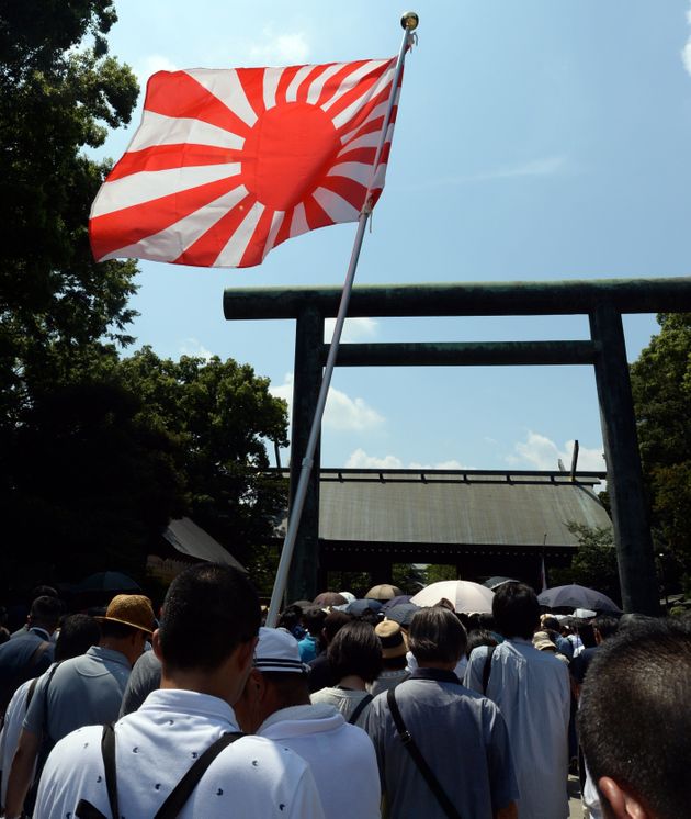 A Rising Sun flag is hoisted as people enter the controversial Yasukuni shrine to honour the dead to mark the 70th anniversary of Japan's surrender in World War II in Tokyo on August 15, 2015. Japan marked the 70th anniversary of the end of the World War II on August 15 under criticism from neighbours China and South Korea which said Prime Minister Shinzo Abe's speech the day before failed to properly apologise for Tokyo's past aggression.         AFP PHOTO / TOSHIFUMI KITAMURA        (Photo credit should read TOSHIFUMI KITAMURA/AFP/Getty Images)
