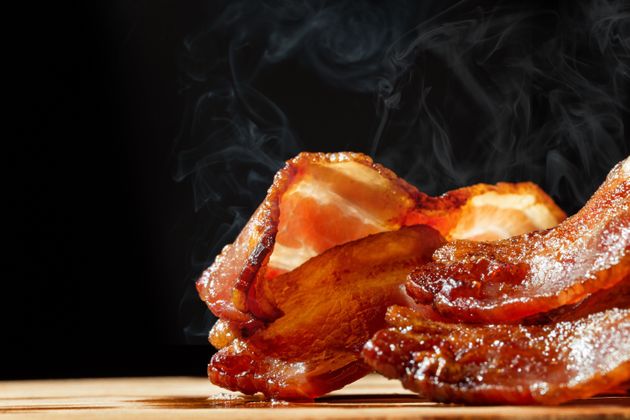 Closeup of slices of crispy hot freshly cooked bacon with copy space in black background