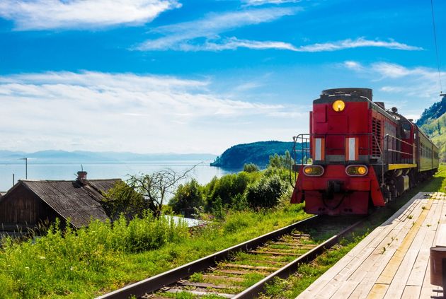 Landscape for travel with the arrival of a red train on a wooden deserted platform Circum-Baikal railway in a village on Lake Baikal in a bright summer sunny day.