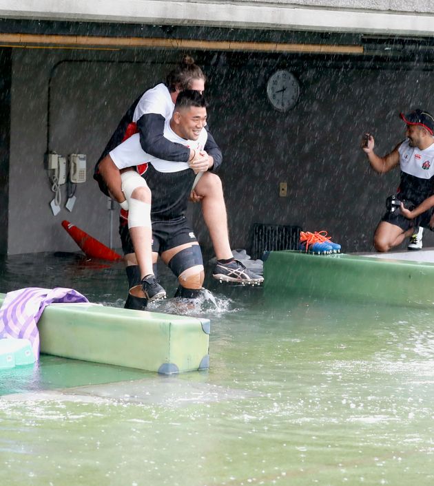 Japan's rugby team player Jiwon Koo, carries teammate James Moore in a flooded walkway at a stadium in Tokyo as the team practices ahead of their match against Scotland, Saturday, Oct. 12, 2019. Tokyo and surrounding areas braced for a powerful typhoon forecast as the worst in six decades, with streets and trains stations unusually quiet Saturday as rain poured over the city. (Yuki Sato/Kyodo News via AP)