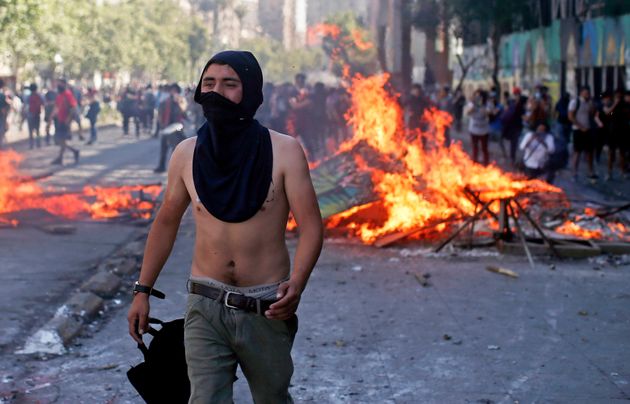 A masked protester walks near a burning barricade during clashes with police in Santiago, Chile, Monday, Oct. 21, 2019. Hundreds of protesters are defying an emergency decree to confront police in Chile's capital, continuing disturbances that have left at least 11 dead and led the president to say the country is 'at war.' (AP Photo/Luis Hidalgo)