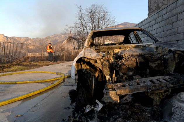 A vehicle lays destroyed from the flames of the Tick Fire while a SoCal Gas worker assesses the damage of a nearby home in Santa Clarita, Calif. on Thursday, Oct. 24, 2019. (AP Photo/ Christian Monterrosa)