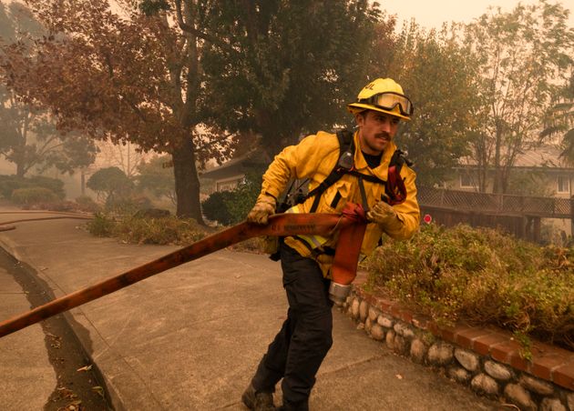 A firefighter pulls a hose as crews work to control the Kincade Fire on Vinecrest Road in Windsor, Calif., on Sunday, Oct. 27, 2019. (AP Photo/Ethan Swope)