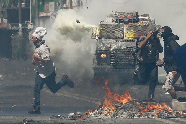 A man wearing a chef's hat runs for cover as anti-government protesters clash with police in Valparaiso, Chile, Thursday, Oct. 24, 2019. President Sebastian Pinera made more economic concessions Thursday announcing a freeze on a 9.2% rise in electricity prices until the end of next year, to try to curb a week of deadly protests over price increases and other grievances. (AP Photo/Matias Delacroix)