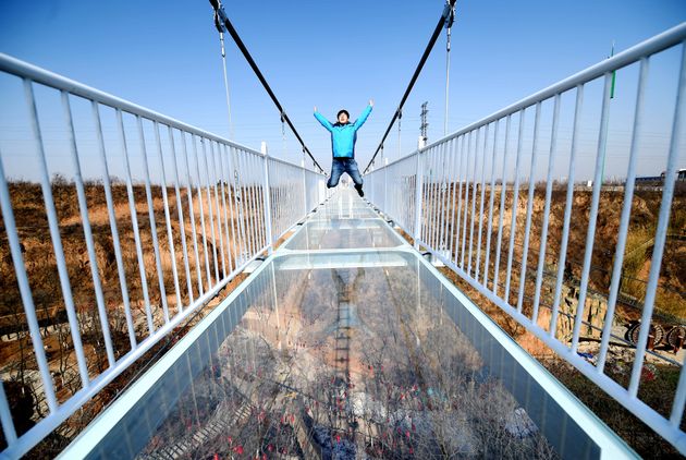 LUOYANG, CHINA - FEBRUARY 07:  Tourists walk on a glass-bottomed skywalk at Yibin District on February 7, 2018 in Luoyang, Henan Province of China. The glass walkway stretches 138 meters into the air with 4D effects. It is said that pedestrians stepping on the skywalk can see blooming peony flowers dotted along the road and hear the sound of glass breaking.  (Photo by Visual China Group via Getty Images/Visual China Group via Getty Images)