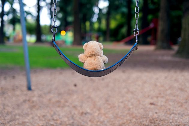 Teddybear sitting alone on a swing set at the park