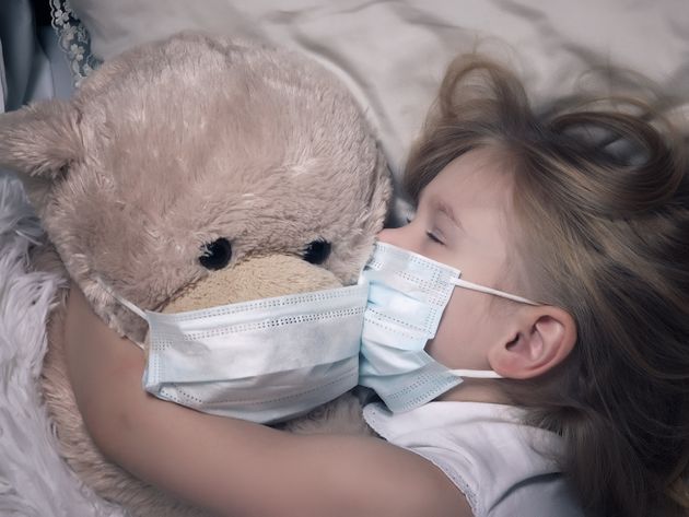 Little girl and big plush bear sleep in medical masks. The concept of childhood diseases, empathy, support and help sick children