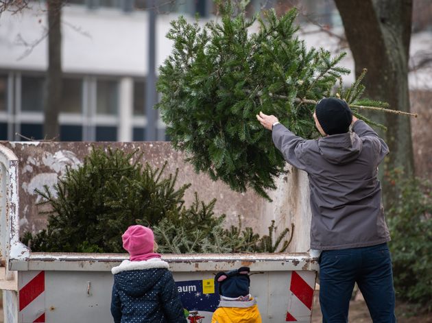 30 December 2019, Saxony, Dresden: A man throws his Christmas tree into a specially erected container while his children watch him. Until 11 January 2020, citizens can dispose of their Christmas trees free of charge. The Department for City Greenery and Waste Management is setting up over 100 collection points throughout the city. Photo: Robert Michael/dpa-Zentralbild/dpa (Photo by Robert Michael/picture alliance via Getty Images)