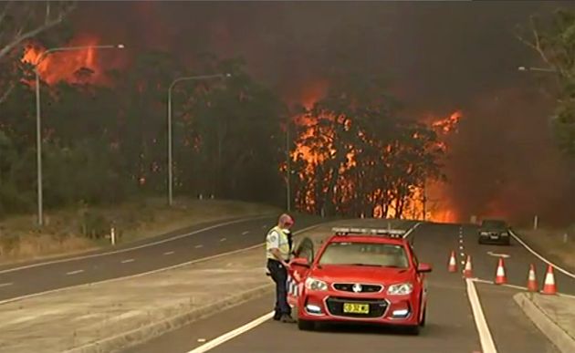 In this image made from video, officials block the Princes Highway as wildfires approach in South Coast, New South Wales Australia, Tuesday, Dec. 31, 2019. Wildfires burning across Australia's two most-populous states have trapped residents of a seaside town in apocalyptic conditions, destroyed many properties and caused fatalities. 
 (Australian Broadcasting Corporation, Channel 9, Channel 7 via AP)