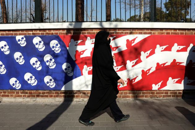 A mourner walk back from a funeral ceremony for Iranian Gen. Qassem Soleimani and his comrades, who were killed in Iraq in a U.S. drone attack on Friday, passing graffiti on the wall of the former U.S. Embassy in Tehran, Iran, Monday, Jan. 6, 2020. A push led by pro-Iran factions to oust U.S. troops from Iraq is gaining momentum, bolstered by a Parliament vote in favor of a bill calling on the the government to remove them. But the path forward is unclear. (AP Photo/Vahid Salemi)