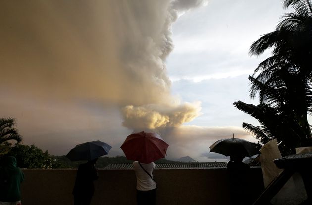 People watch as Taal Volcano erupts Sunday Jan. 12, 2020, in Tagaytay, Cavite province, outside Manila, Philippines.  A tiny volcano near the Philippine capital that draws many tourists for its picturesque setting in a lake belched steam, ash and rocks in a huge plume Sunday, prompting thousands of residents to flee and officials to temporarily suspend flights. (AP Photo/Aaron Favila)