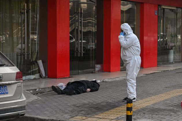 EDITORS NOTE: Graphic content / This photo taken on January 30, 2020 shows officials in protective suits checking on an elderly man wearing a facemask who collapsed and died on a street near a hospital in Wuhan. (Photo by Hector RETAMAL / AFP)