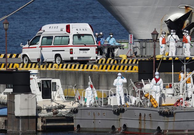 Workers in protective gear are seen next to a waiting ambulance at the Japan Coast Guard base in Yokohama on February 5, 2020, to bring the patients from the Diamond Princess cruise ship which remains offshore at the port. - At least 10 people on a cruise ship quarantined off the coast of Japan have tested positive for the new coronavirus, Japan's health minister said on February 5. (Photo by STR / JIJI PRESS / AFP) / Japan OUT (Photo by STR/JIJI PRESS/AFP via Getty Images)