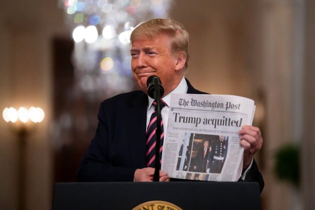 President Donald Trump holds up a newspaper with a headline that reads 'Trump acquitted' as he speaks in the East Room of the White House, Thursday, Feb. 6, 2020, in Washington. (AP Photo/Evan Vucci)