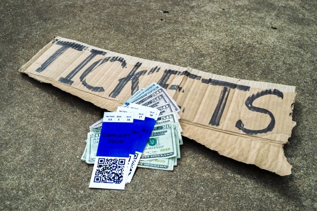 A concert ticket scalper's ticket stubs with QR code, money  and his cardboard sign with 'TICKETS' written on it  sitting on the concrete.