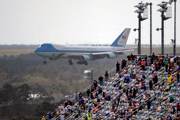 Fans watch from the grandstands as Air Force One, carrying President Donald Trump, prepares to land at Daytona International Airport before the NASCAR Daytona 500 auto race at Daytona International Speedway, Sunday, Feb. 16, 2020, in Daytona Beach, Fla. (AP Photo/Phelan M. Ebenhack)