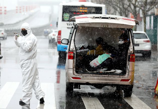 A worker in protective suit stands amid snow to help transport novel coronavirus patients outside a hospital, in Wuhan, Hubei province, China February 15, 2020. China Daily via REUTERS  ATTENTION EDITORS - THIS IMAGE WAS PROVIDED BY A THIRD PARTY. CHINA OUT.