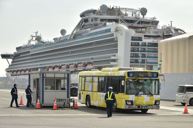 A bus carrying passengers who disembarked from the Diamond Princess cruise ship (back), in quarantine due to fears of the new COVID-19 coronavirus, leaves the Daikoku Pier Cruise Terminal in Yokohama on February 20, 2020. - Japan hit back at criticism over 'chaotic' quarantine measures on the coronavirus-riddled Diamond Princess cruise ship, as fears of contagion mount with more passengers dispersing into the wider world. (Photo by Kazuhiro NOGI / AFP) (Photo by KAZUHIRO NOGI/AFP via Getty Images)