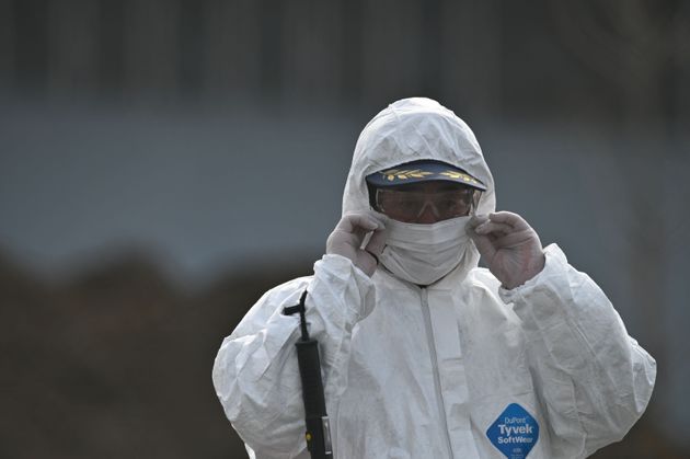 A worker in protective clothes puts on his face mask as he walking near by the Diamond Princess cruise ship, in quarantine due to fears of new COVID-19 coronavirus, at Daikoku pier cruise terminal in Yokohama on February 20, 2020. - Japan hit back at criticism over 'chaotic' quarantine measures on the coronavirus-riddled Diamond Princess cruise ship, as fears of contagion mount with more passengers dispersing into the wider world. (Photo by Philip FONG / AFP) (Photo by PHILIP FONG/AFP via Getty Images)