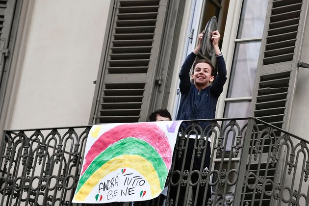 한 어린이가 발코니에 나와 냄비 뚜껑으로 연주를 하고 있다. '모든 게 좋아질 거야'라고 적힌 배너가 난간에 걸려있다. 토리노, 이탈리아. 2020년 3월13일.