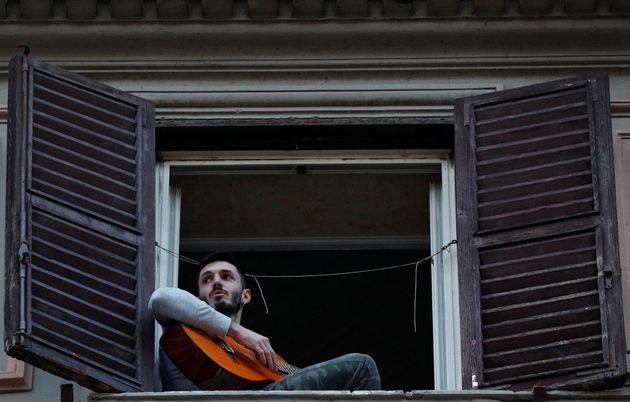 한 남성이 창틀에 걸터앉아 기타를 연주하고 있다. 로마, 이탈리아. 2020년 3월13일.