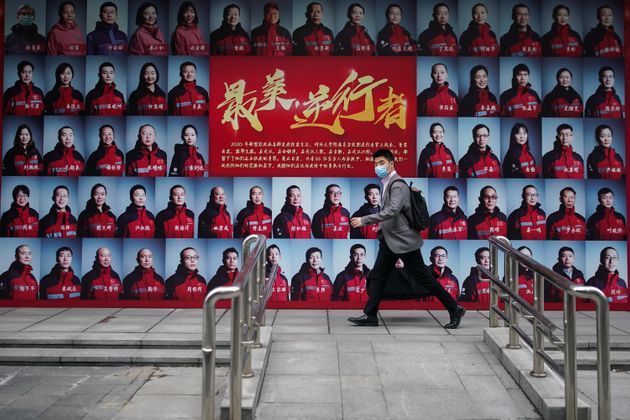 마스크를 착용한 한 남성이 최전선에서 코로나19에 대응한 의료진들의 얼굴이 그려진 포스터 앞을 지나가고 있다. 우한, 중국. 2020년 4월21일.