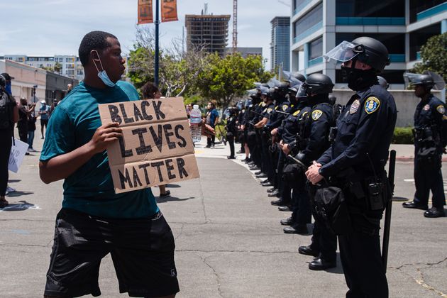 한 시위자가 '흑인의 목숨은 중요하다'는 문구가 적힌 팻말을 들고 경찰과 대치하고 있다. 미국 전역에서는 경찰의 과잉 법 집행으로 흑인이 목졸려 숨지는 사건에 항의하는 시위가 엿새째 이어졌다. 샌디에이고, 캘리포니아주. 2020년 5월31일.