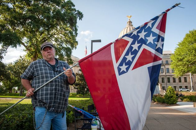 한 시위자가 미시시피 주 의사당 앞에서 주 깃발을 흔들고 있다. 잭슨, 미시시피주. 2020년 6월28일.